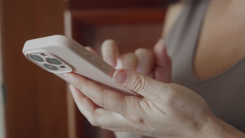 Caucasian woman hands typing text holding white modern smartphone with triple camera in closeup view on blurred background, symbolizing digital communication and mobile technology.