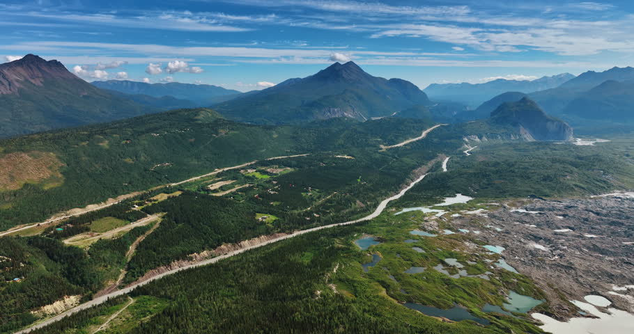 Spectacular green valley crossed by roads. Drone flight approaching the area with multiple puddles. Mountains at backdrop. Alaska, USA.