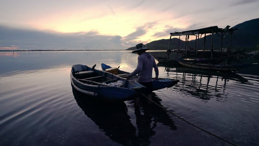 Hue, Vietnam - July 5th, 2025: The silhouette of a fisherman boarding a boat to go fishing in a lagoon at dawn in central Vietnam