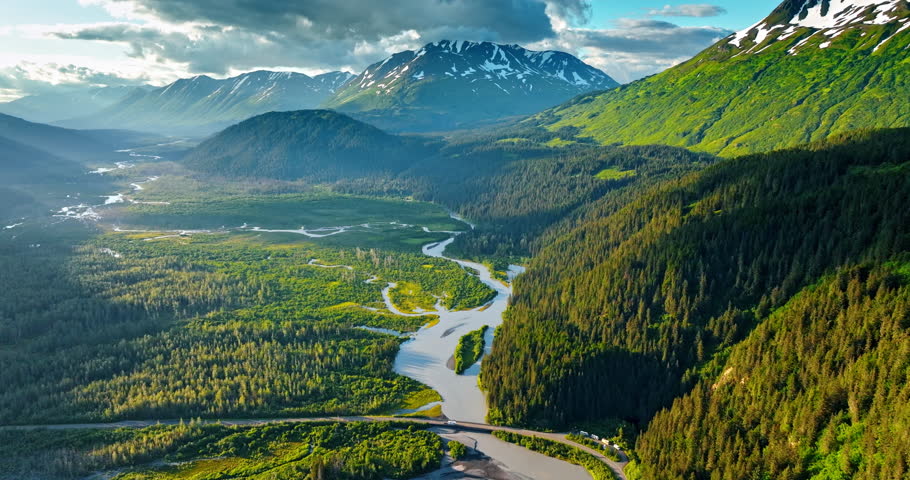 Beautiful green pine tree woods covering the mountains and vast valley. Branching river flows in the valley. Grey cloudscape hang in the sky over the rocks. Alaska, USA.