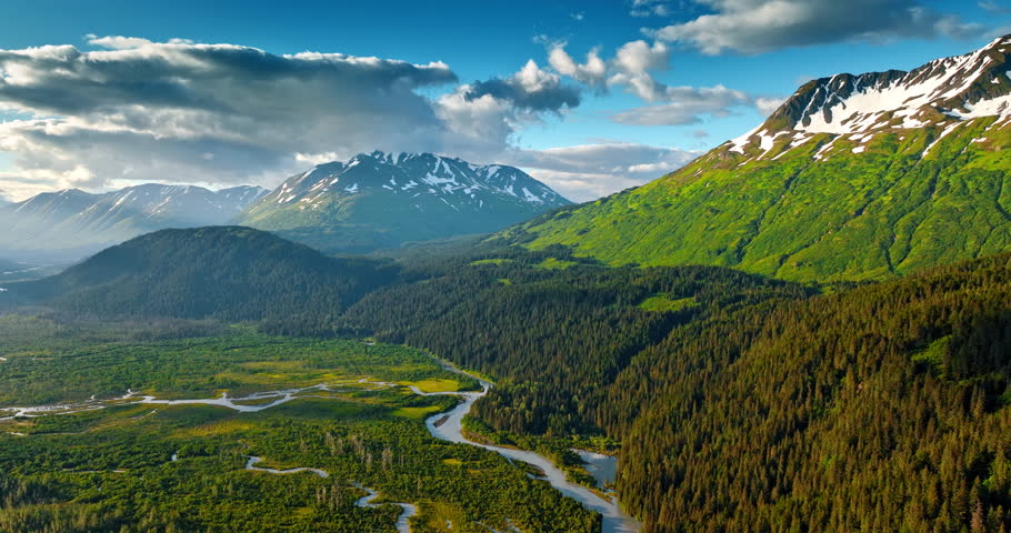 Fantastic nature landscape of beautiful Alaska, USA. Valley with branching river, pine tree woods and snow-capped mountains from drone footage.
