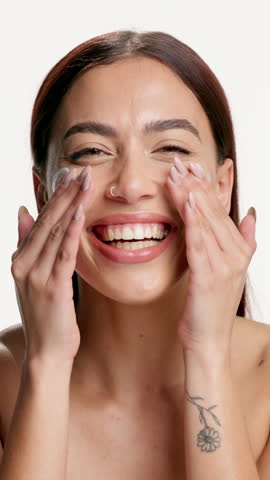 Beauty, woman and apply face cream in studio for skincare routine, acne treatment or wellness. Hyaluronic acid, girl and happy with moisturizer on white background for healthy skin, results and glow