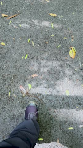 Hikerâs legs and boots walking on damp, leaf-strewn trail, natural daylight, steady downward view