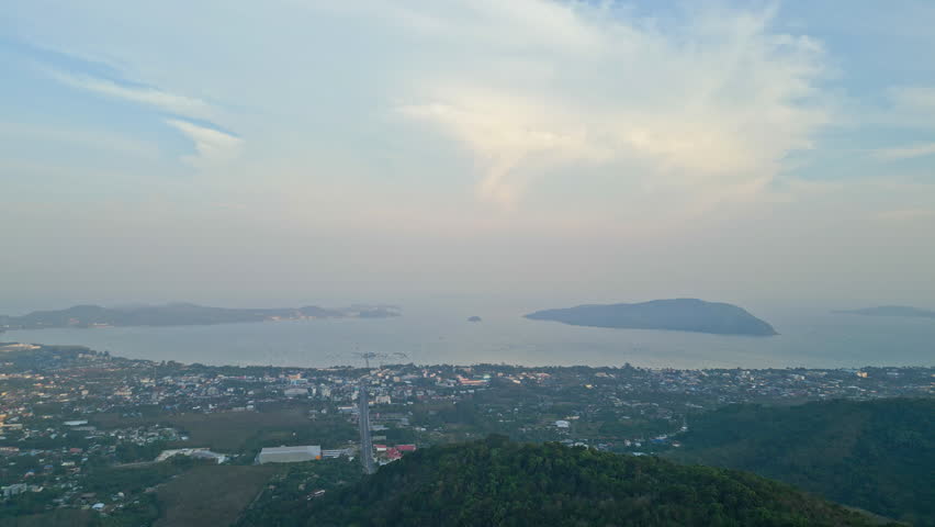 Wide aerial panorama over Phuket Town and the surrounding bays at dusk with soft pastel clouds and hazy distant islands.