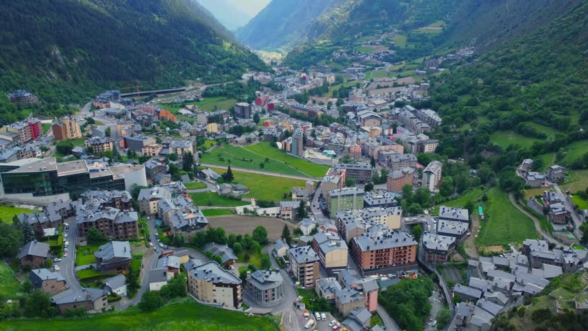 aerial shot showcasing the picturesque town of Encamp, nestled within a lush valley of the Pyrenees mountains in Andorra. The footage captures the charming architecture, winding roads, and surrounding
