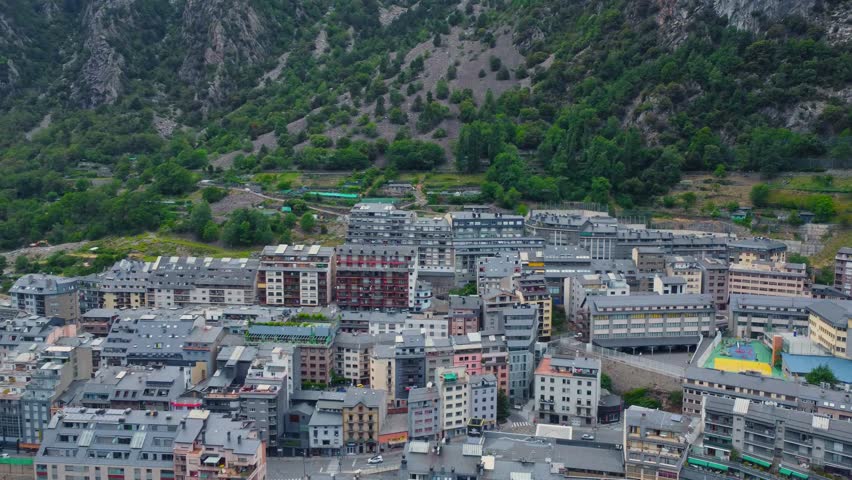 aerial drone shot showcasing the dense urban landscape of Andorra la Vella nestled within the majestic Pyrenees mountains. This footage captures the unique blend of modern architecture and stunning na