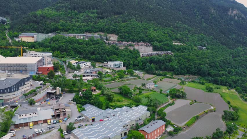 This aerial footage captures the picturesque landscape of Andorra, showcasing the dramatic Pyrenees mountains alongside modern urban development. The drone perspective reveals a mix of lush green fore
