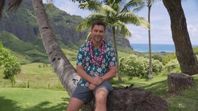 Male tourist sits under a palm tree wearing a Hawaiian shirt and flower lei with ocean and mountains in the background. The scene captures the spirit of Aloha, relaxation, and tropical island travel - Powered by Shutterstock - Get 15% off with code: PIKWIZARD15