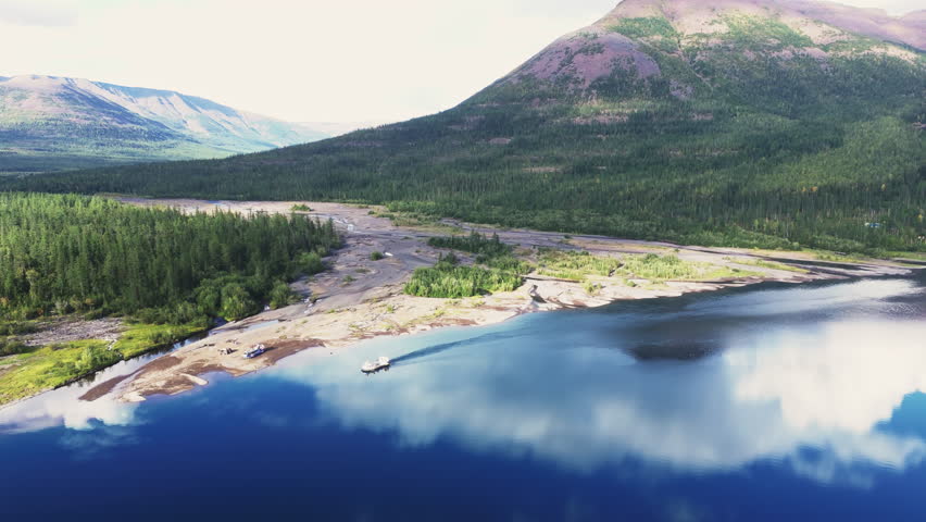 River mouth and delta sandbar reflect white cloud on calm Lake Lama within the Putorana Plateau. Base camp and tiny pier hint at access to a vast UNESCO wilderness in late summer daylight