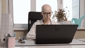 Bald woman with cancer smiling while working on laptop at home office, remote job, online education, chemotherapy survivor using computer - Powered by Shutterstock - Get 15% off with code: PIKWIZARD15