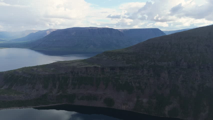 Layered basalt cliff rises above Lake Lama in the heart of the Putorana Plateau. Moody light and high wall show the unique trap landscape and Arctic frontier character in late afternoon