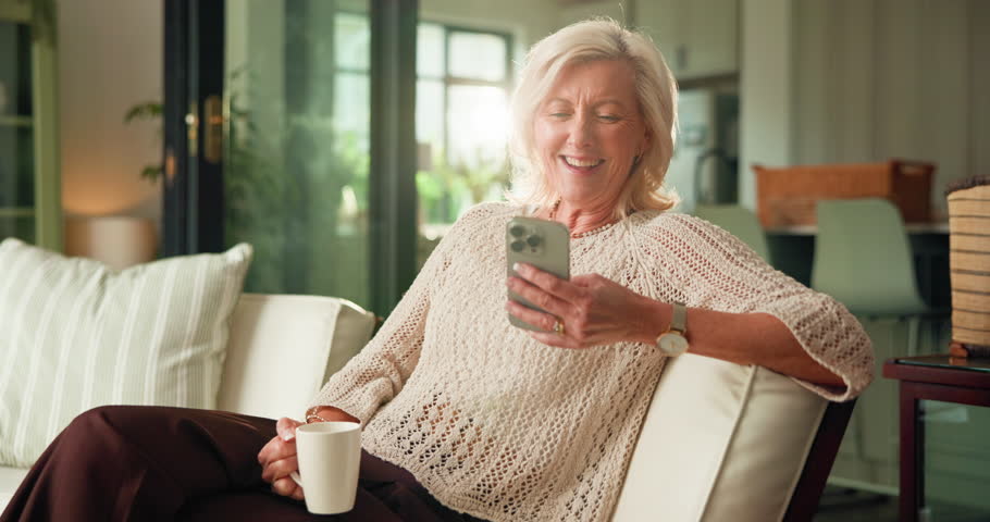 Phone, laughing and coffee with old woman on sofa for relax, social media meme and morning drink. Happiness, online funny video and drinking tea with senior person in living room of home for post