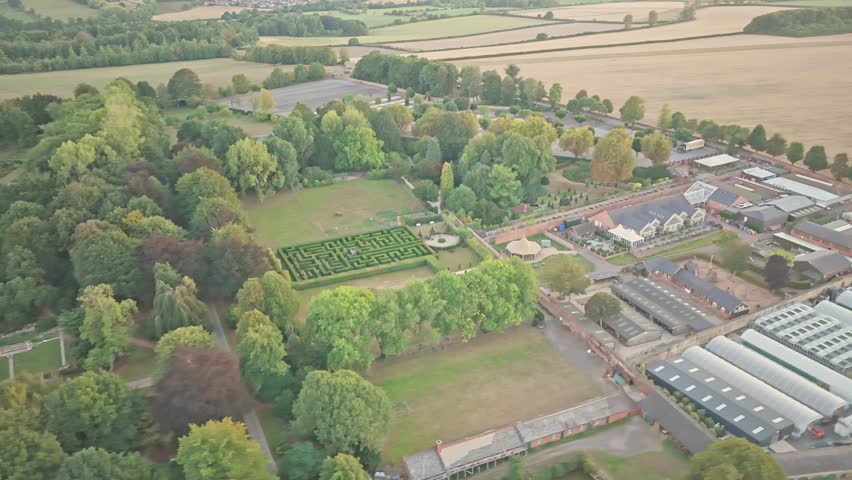 Orbiting drone shot reveals Wentworth Woodhouse unfolds with circular motion around its garden maze, stone buildings, and tree-lined fields, framed by golden light and rural geometry.
