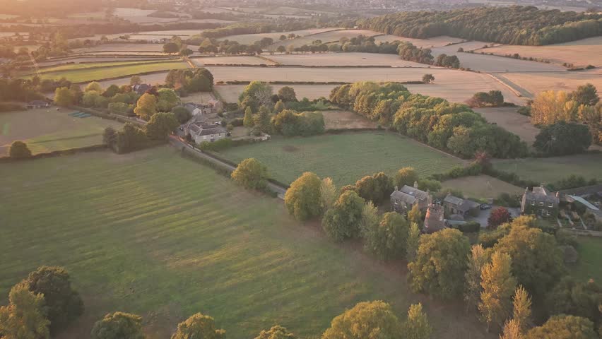 rom a golden-hour push-in, Wentworth Castle rises among trees and fields, with stone towers, pitched roofs, and landscaped lawns framed by rolling terrain and historic countryside.