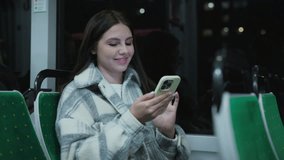 Caucasian woman with long dark hair wearing warm plaid coat sitting alone on bus. Female smiling while holding smartphone and chatting online during evening ride. Social media remote communication. - Powered by Shutterstock - Get 15% off with code: PIKWIZARD15