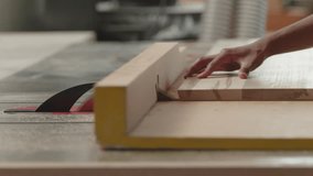 A craftsperson uses a table saw to cut a piece of wood in a busy workshop. The workspace is filled with tools, and the focus is on precision and skill. - Powered by Shutterstock - Get 15% off with code: PIKWIZARD15