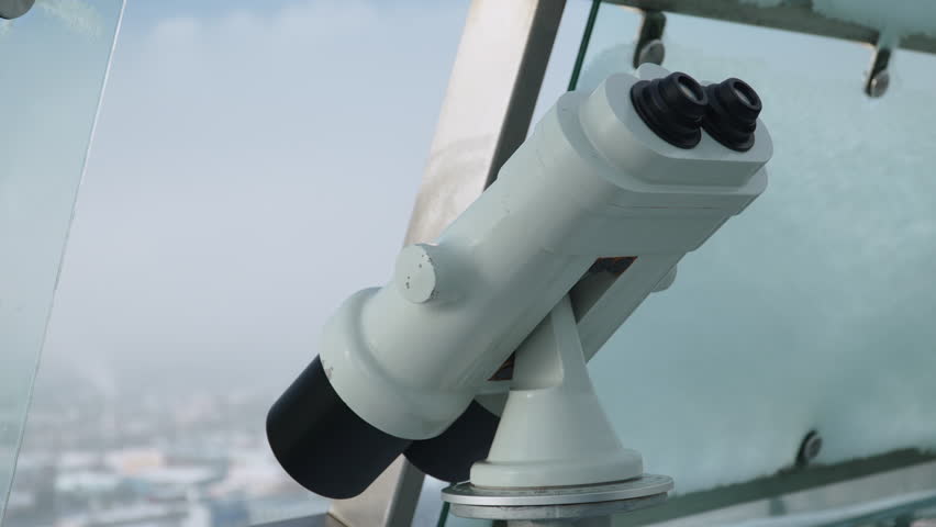 Binoculars on observation deck. Happy woman in winter clothes takes equipment and looks into distance at cityscape. Winter travel.