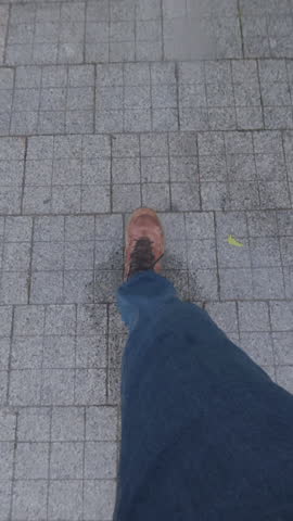 Time lapse, View from above on man's feet in jeans and boots walking hastily on wet granite pavement sidewalk, first person view. POV: person's legs fast going in rainy weather on damp paved pavement