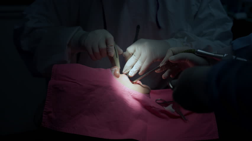A team of professional dentists and oral surgeons perform a dental surgery in a sterile, modern operating room.