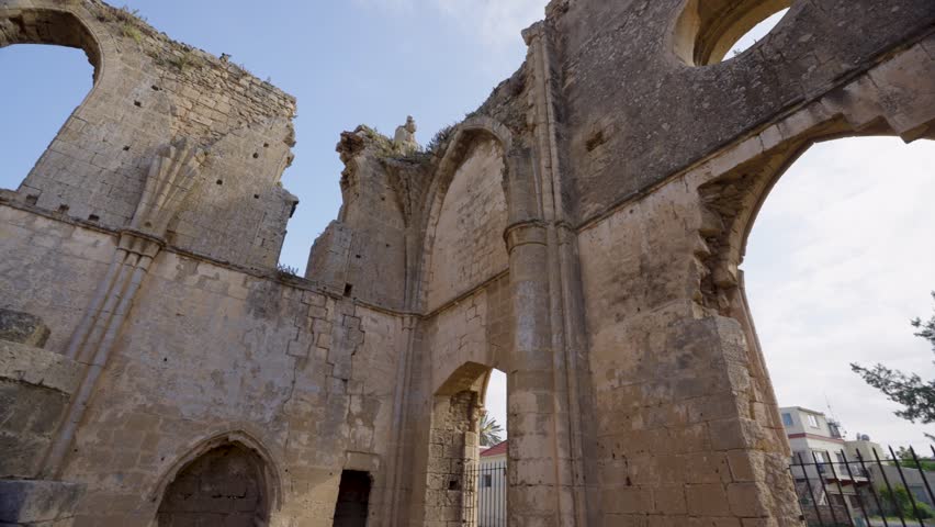 Ruins of a historic church in Northern Cyprus, showing ancient stone architecture, arched windows, and detailed masonry under a clear blue sky