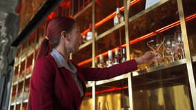 Female bartender wiping and polishing glasses arranged on shelves behind the bar counter, preparing for opening time, representing hospitality service. Restaurant business lifestyle concept. - Powered by Shutterstock - Get 15% off with code: PIKWIZARD15