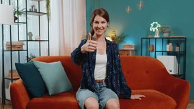 Portrait of excited smiling Caucasian woman looking approvingly at camera showing double thumbs up, like sign, good news, positive feedback. Happy young girl sitting on sofa in living room at home. - Powered by Shutterstock - Get 15% off with code: PIKWIZARD15