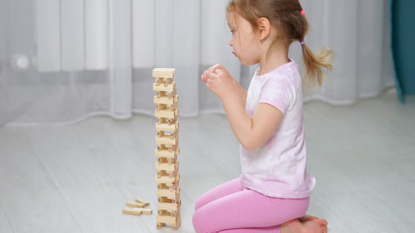 Young girl carefully placing wooden blocks, building a tall tower on the floor in a bright room