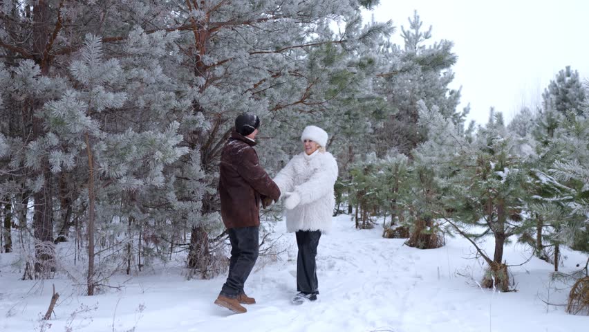 Romantic senior couple holding hands and walking together through a beautiful snowy forest. Happy mature man and woman enjoying a walk in winter - Powered by Shutterstock - Get 15% off with code: PIKWIZARD15