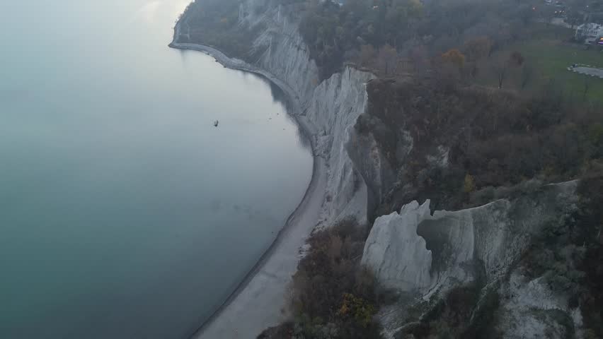 Wide aerial view of Bluffer’s Park beach beneath the Bluffs under soft light; lake, sand, and cliffs. Use for travel and tourism visuals