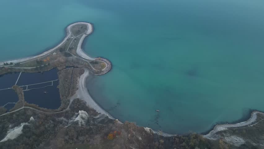 Aerial capture of beach at Bluffer’s Park with lake waters, pale sky, and cliffs silhouetted by soft light. Great for romantic or peaceful scenic clips
