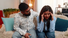 Indian couple man and woman sitting on home sofa, girl suffering from headache while guy gently massages her shoulders with care. Young family supporting each other with love, comfort emotional warmth - Powered by Shutterstock - Get 15% off with code: PIKWIZARD15
