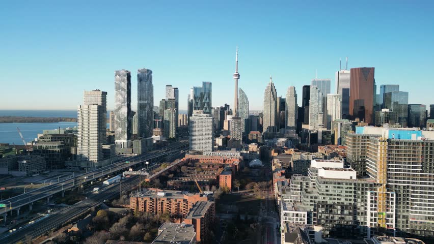 Wide 4K drone shot of downtown Toronto skyline under bright blue sky — CN Tower standing tall among modern buildings. Perfect for travel videos, real estate promos, and city branding