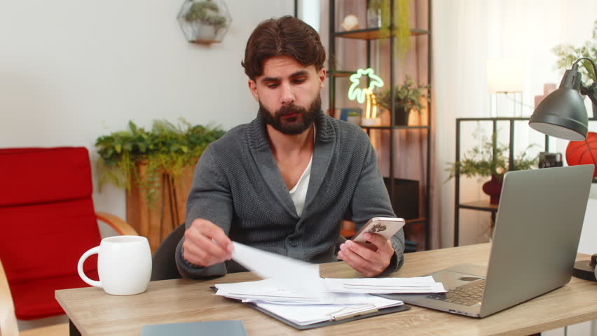 Indian man at home audits bills with smartphone runs finger on rows finds wrong card charge and flags issue. Arabian guy at desk checks payments cancels order shows anger plans dispute bank support.