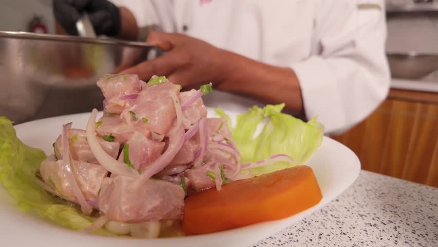Professional chef in a restaurant kitchen plating a traditional peruvian ceviche. Delicious raw fish dish with onions, lime, and lettuce