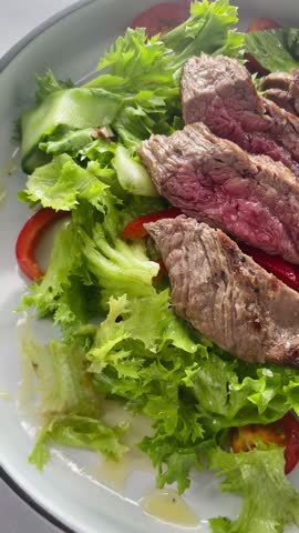 A tasty salad with sliced steak on a fresh bed of crisp lettuce and vibrant tomatoes, served in a stylish bowl