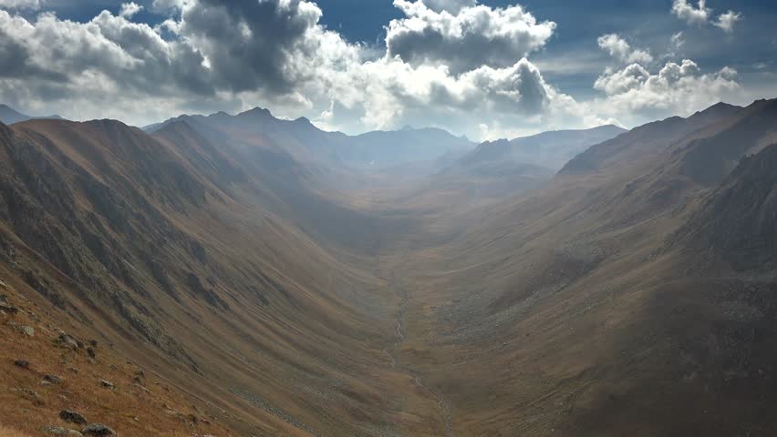 Time-lapse view of a treeless U-shaped valley in the Chilean Andes. Glacially carved slopes and high-altitude ridges reveal rugged Patagonian scenery under drifting clouds.