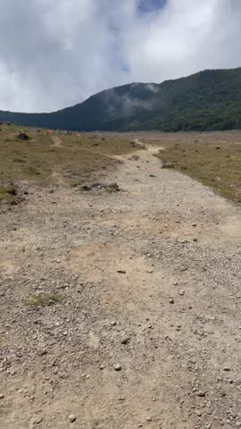 Winding Dirt Path Ascending a Grassy Slope Towards Misty Mountains Under a Cloudy Sky
