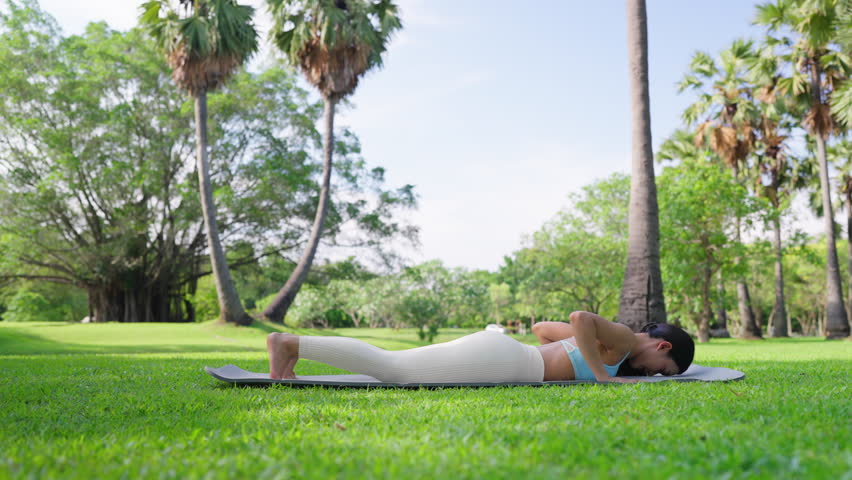 Caucasian slim body standing in yoga position downward facing dog on fitness mat, slimming, young Asian woman stretching outdoors in park