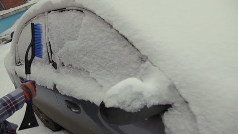 Car in snow, woman cleans snow from car