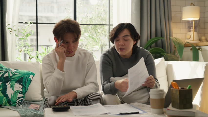 "Asian LGBTQ male couple reviews monthly financial bills and household expenses together at home, managing shared budget planning, savings goals and responsible money management for their future 