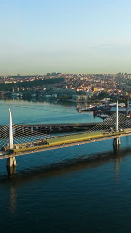 Vertical video. Istanbul, Turkey. Golden Horn Metro Bridge and Halic Station pedestrian crossing illuminated by morning sun over the bay. Aerial View, Point of interest. Rich colors