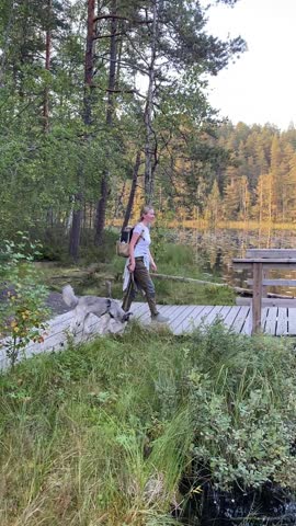 Woman walking with dog on wooden bridge at Haukkalampi lake in Nuuksio National Park Finland