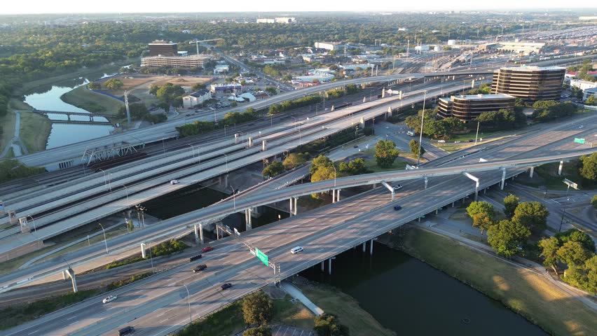 Stacked highway interchange spans Trinity River, flanked by office buildings, campus zones, rail tracks, industrial corridors. Green buffer, paved trails reflect Fort Worth layered urban planning. USA