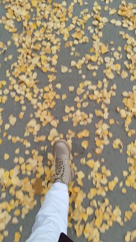 person legs going on the autumn road with yellow foliage. Cozy video.