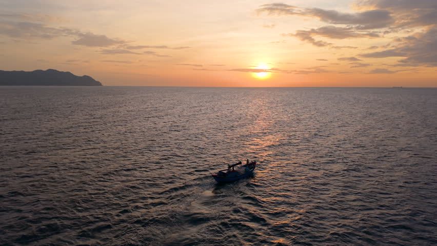 Aerial drone shot of Vietnam fishing boat, moving on tropical sea waves under sunrise sky. Royalty high-quality free best stock of fishermen’s heading offshore in calm ocean waves, cultural seascape