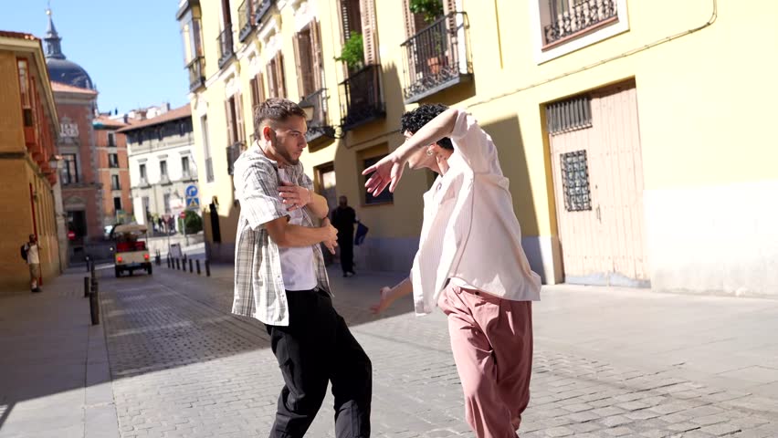 Two talented young male dancers performing a contemporary and expressive dance routine on a sunny cobblestone street, showcasing their fluid movements and artistic collaboration in an urban setting