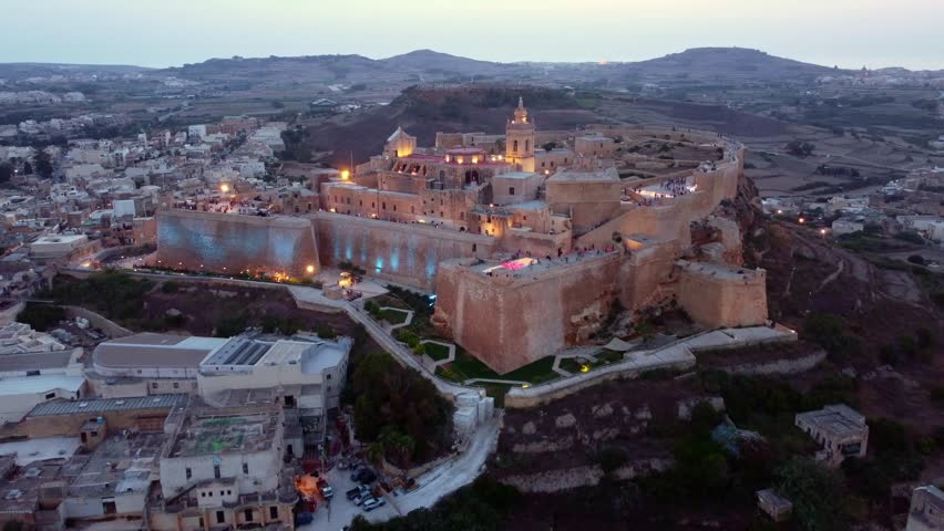 4K drone flight approaches the illuminated Citadella in Rabat, Gozo at dusk during the Light Festival: glowing ramparts, cathedral domes and visitors create a cinematic cultural and travel showcase