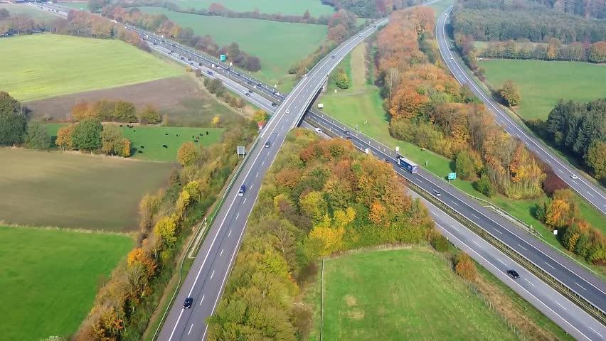 Cars and trucks driving through a complex highway interchange in the german countryside surrounded by colorful autumn forests and green fields