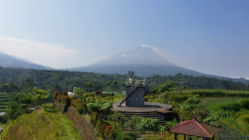 A breathtaking view of a majestic mountain range from an observation tower surrounded by lush greenery and clear blue skies.