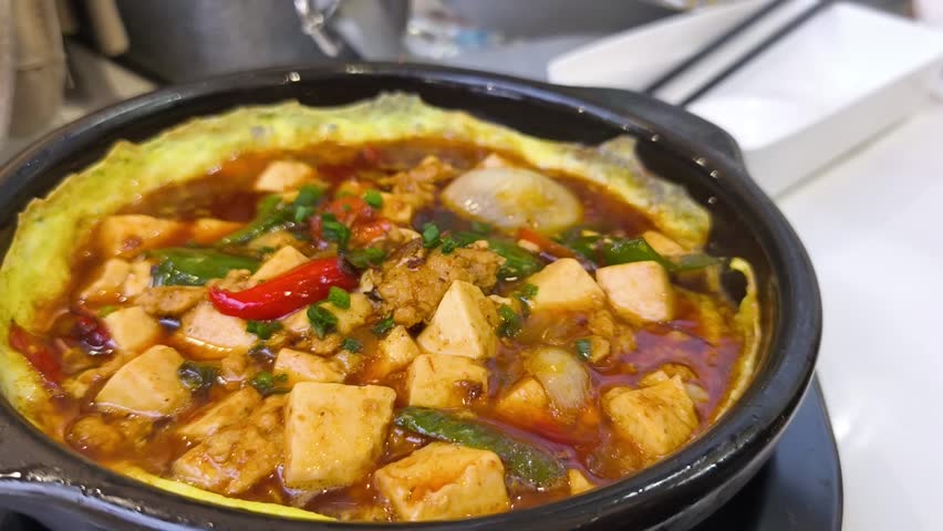 Chopsticks lifting minced meat and tofu from a sizzling clay pot with egg.